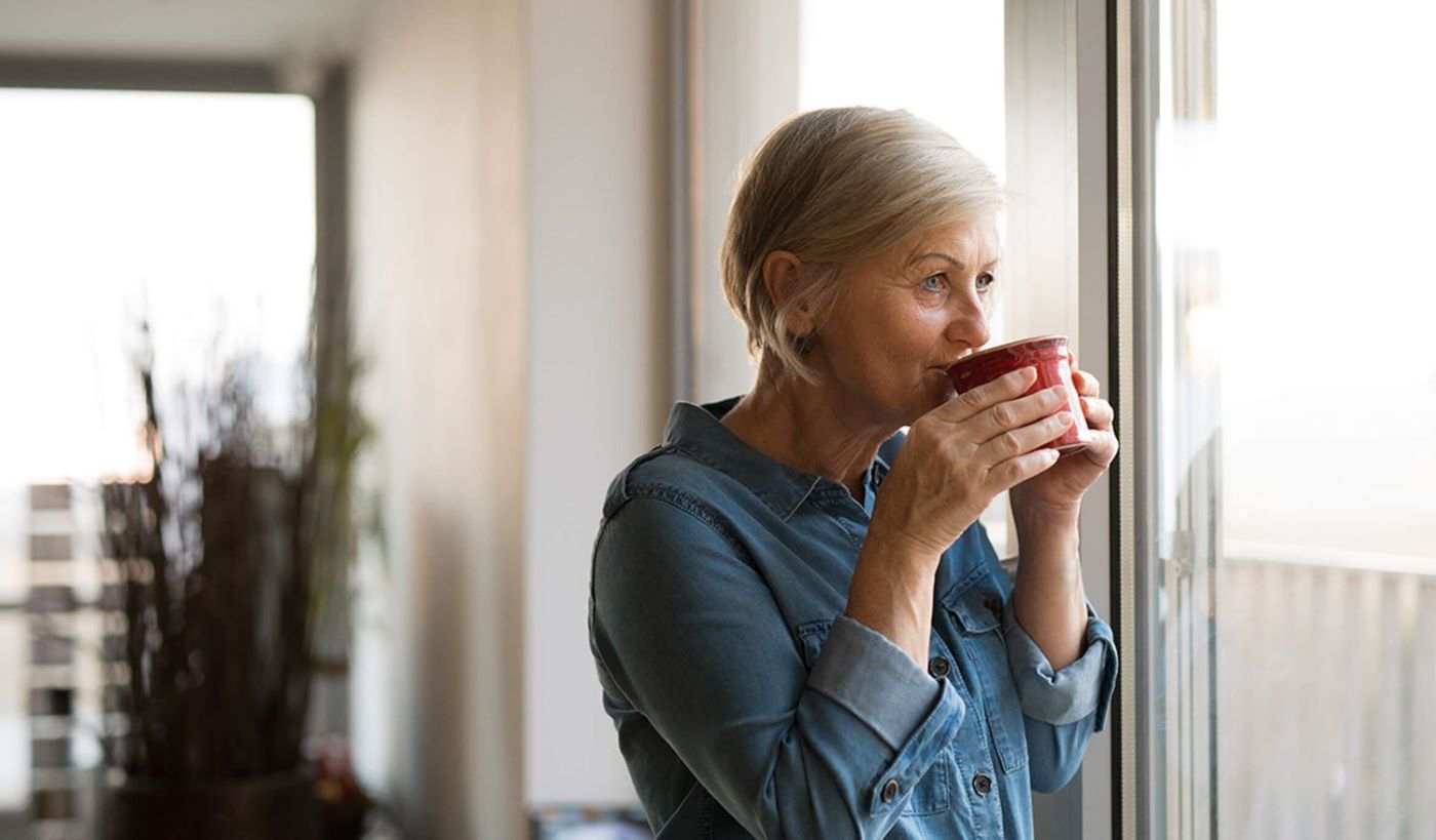 Woman looking out window sipping mug