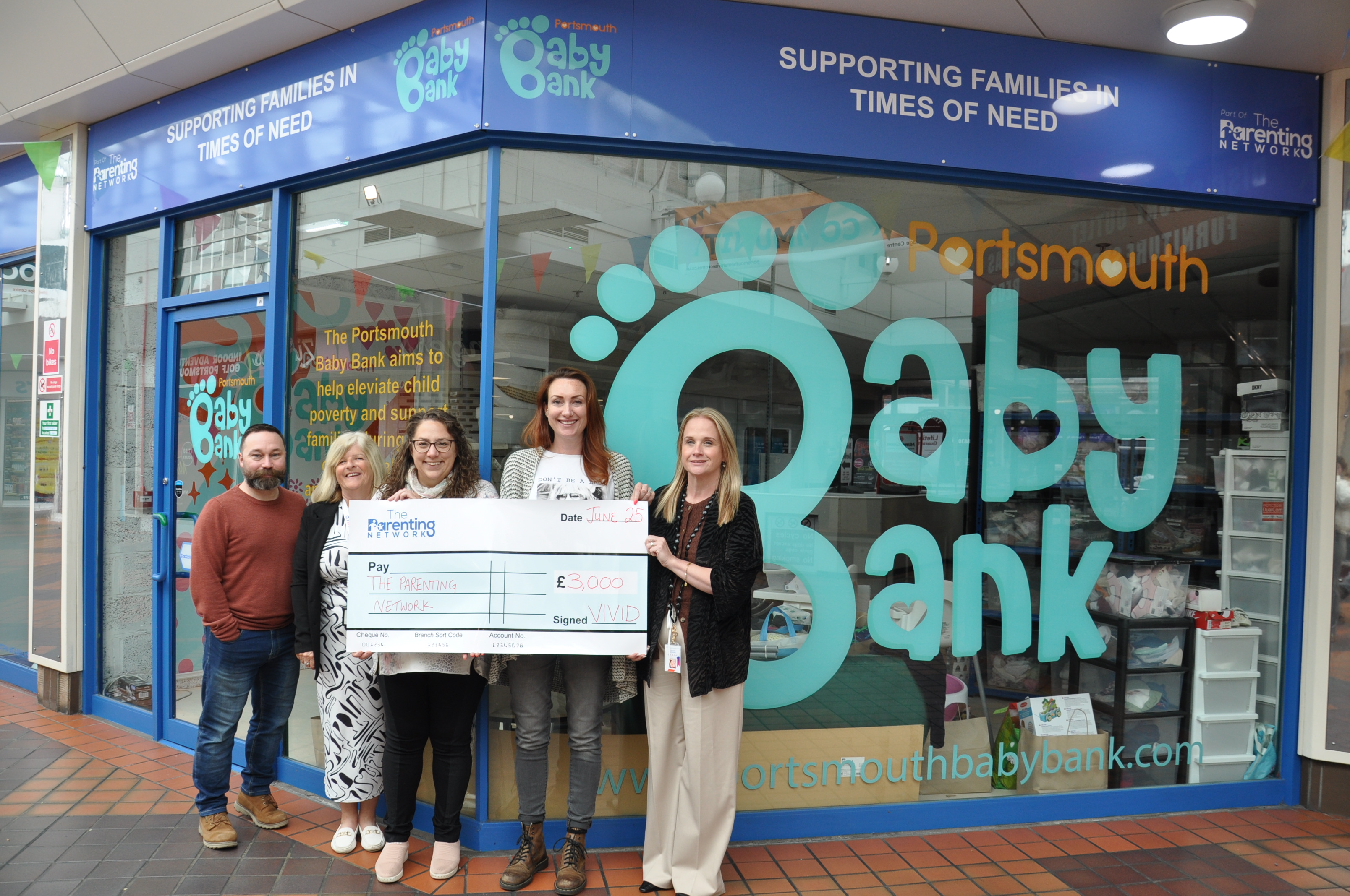 5 people stood outside baby bank centre holding cheque