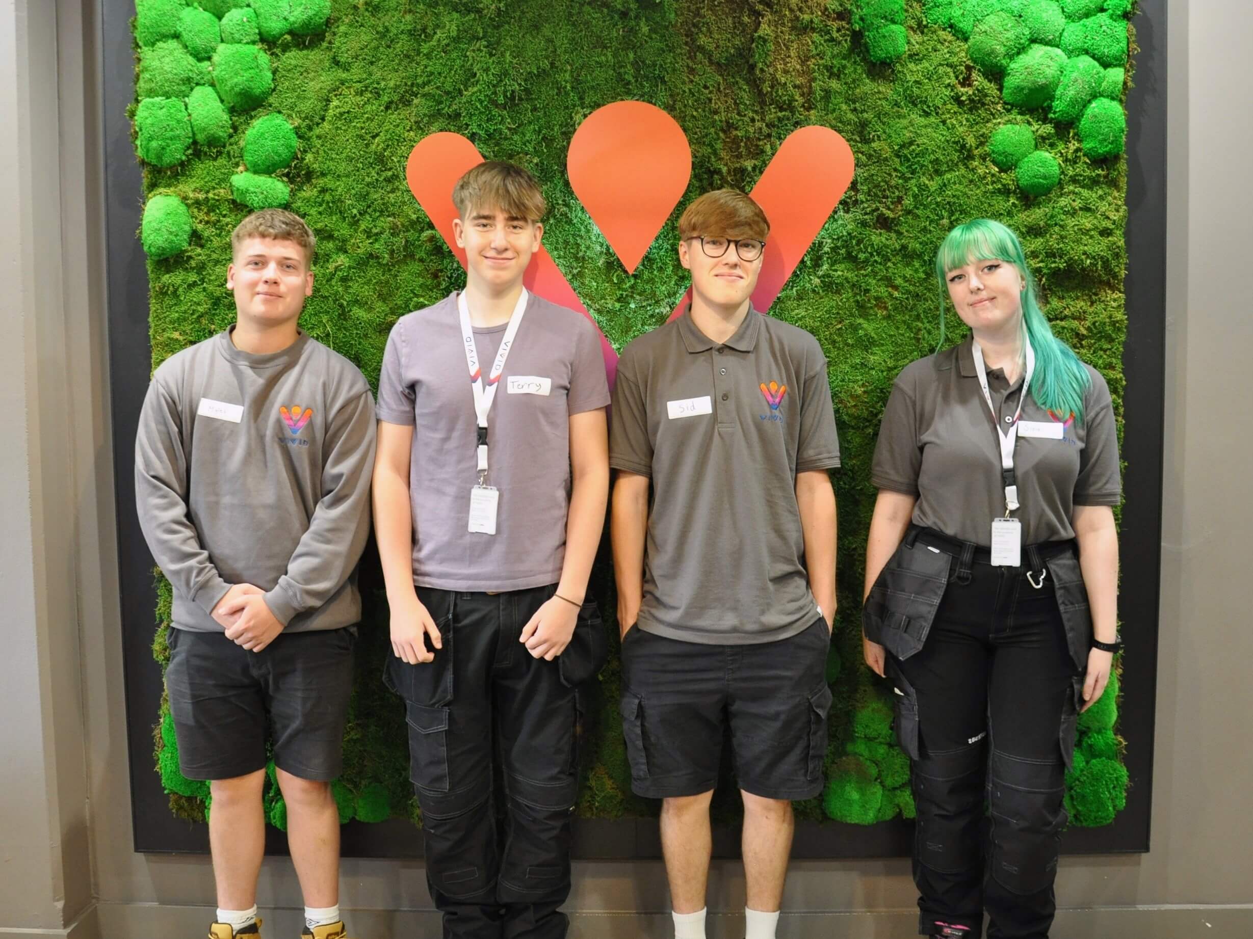 Four electrician apprentices standing in front of living wall with VIVID logo