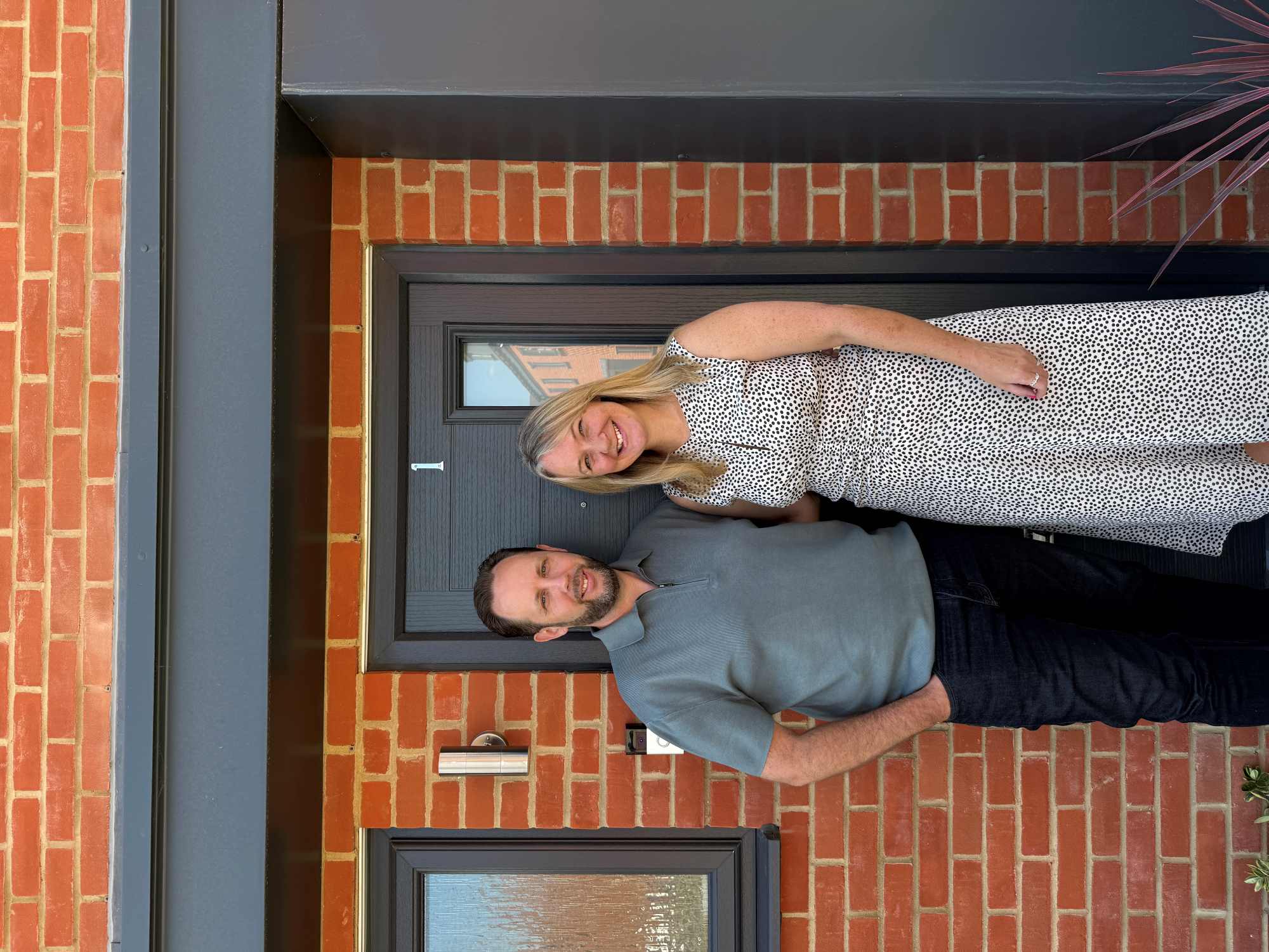 Two people smiling in front of house